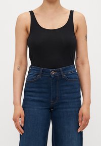 Musta hihaton toppi, jossa on sileä pinta, yhdistettynä korkeavyötäröisiin sinisiin farkkuihin, joissa on nappisuljenta ja huomaamaton ompelu.