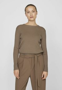 Brązowy sweter z prążkowanego dzianiny z długim rękawem, zestawiony z spodniami w kolorze brązowym o wysokim stanie i detalem w postaci materiałowego paska. Prosty, dopasowany fason.