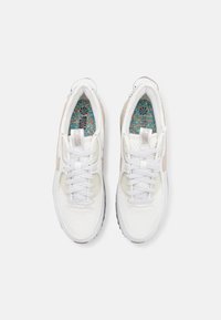 Ett par vita sportiga sneakers med mesh-detaljer, vita snören och färgglada mönstrade innersulor, visade från ovan på en vit bakgrund.