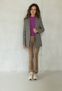 Grijze geruite blazer over een paarse top, gecombineerd met beige flare-broek en lichtgekleurde sneakers. Gladde texturen en gestructureerd ontwerp.