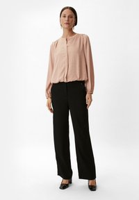 Jasnoróżowa bluzka z długim rękawem, o teksturowanej tkaninie i z zapięciem na guziki, w zestawieniu z czarnymi spodniami o szerokich nogawkach oraz czarnymi, kwadratowymi szpilkami.