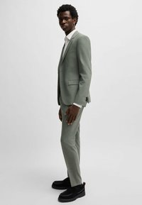 Un costume gris clair au design slim, en tissu texturé, avec des revers crantés. Associé à une chemise blanche et des mocassins noirs à semelles épaisses.