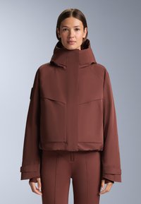 Barna szigetelt dzseki magas gallérral és széles ujjakkal, sima textúrával és hangsúlyos első zsebekkel.