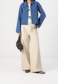 Veste en denim bleu clair avec une coupe courte et fermeture par nœud. Associée à un pantalon ample crème et des chaussures imprimé léopard. Sac à main marron.