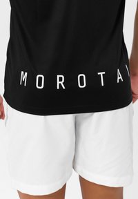Musta urheilupaita, jossa on valkoinen "MOROTAI" -teksti helmapuolella, yhdistetty valkoisiin shortseihin. Materiaali vaikuttaa sileältä ja kevyeltä.