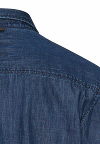 Mørkeblå denimstof med synlige sømme langs ryg-ykken og kravesømmen på en skjorte.