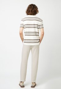 T-shirt in cotone a righe nei toni crema e marrone, abbinato a pantaloni leggeri beige. Presenta una vestibilità comoda e maniche corte. Calzature casual completano il look.