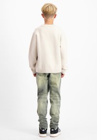 Lichtbeige gebreide trui met ribbelmouwen en onderrand, gecombineerd met vervaagde groene jeans en zwarte sneakers met witte zolen. Achteraanzicht.