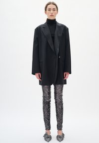 Črn oversized blazer, črn pulover s prstanom, hlače s srebrnimi in črnimi bleščicami, sivo zavezane balerinke; gladek material, strukturirana zasnova, ohlapen kroj.