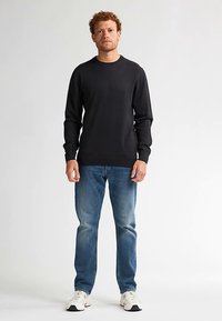 Zwarte katoenen sweatshirt met lange mouwen, ronde hals, losse pasvorm, gecombineerd met blauwe denim jeans en witte sneakers. Eenvoudig ontwerp, zonder patronen.