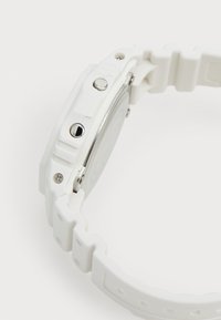 Montre en silicone blanche avec un cadran rectangulaire, des boutons métalliques et un bracelet texturé. Les détails notables incluent des vis et une surface arrière lisse.