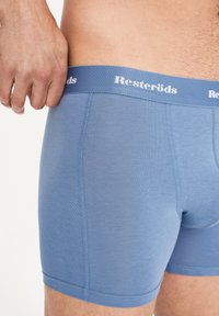 Světle modré látkové boxerky s jemnou texturou, s elastickým pasem označeným značkou "Resteröds" v bílé barvě.