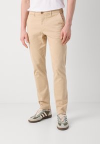 Beige chinos med rett snitt, laget av glatt stoff. Har knappelukking og sidelommer, kombinert med grå og grønne joggesko.