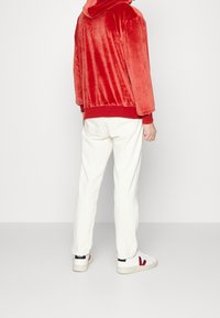Sudadera de terciopelo rojo suave con capucha, puños elásticos y dobladillo, combinada con pantalones rectos crema y zapatillas blancas con un logo rojo.