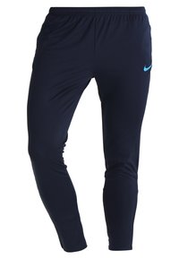 Granatowe spodnie sportowe z elastycznym pasem, zwężanym fasonem, wykonane z gładkiego materiału; z jasnoniebieskim logo Nike po lewej stronie.