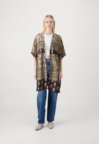 Εξωτερικό ένδυμα σε στυλ κιμονό σε καφέ χρώμα με χρυσά σχέδια, διαθέτει φαρδιές μανσέτες και άνετη εφαρμογή· συνδυασμένο με λευκό τοπ και μπλε τζιν.