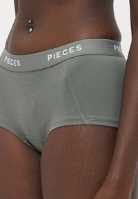 Zeleni donji dio od pamuka s mekim završetkom, s bijelim elastičnim pojasom na kojem je logotip "PIECES" te srednjim dizajnom.