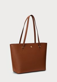 Brun skinn toteveske med en strukturert design, som har to håndtak og en gulllogo på fronten. Glatt tekstur.
