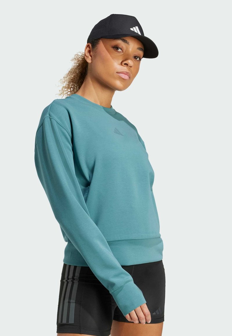 Teal sweatshirt with long sleeves, ribbed hem, and a small logo on the chest. Paired with black shorts featuring three vertical stripes.