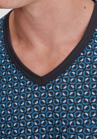 Zwarte V-hals T-shirt met een blauw en lichtblauw cirkelpatroon. Gemaakt van stof met een gladde textuur en een zakdetail.
