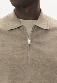 Bežový polo sveter na zips s golierom, vyrobený z jemnej pleteniny. Obsahuje kovový zips a hladký povrch.