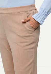 Pantaloni beige a gamba affusolata con finitura testurizzata, tasca laterale e cintura elastica; abbinati a un maglione lavorato a maglia azzurro chiaro con polsini a coste.