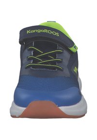 Sininen urheilukenkä, jossa on verkkopintainen yläosa, neonvihreät yksityiskohdat, valkoinen välikerros ja kumipohja. Varustettu säätöremmillä ja nauhoilla.