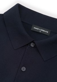 Granatowy polo z prążkowanym kołnierzem, dwoma czarnymi guzikami oraz czarną metką z napisem "PAKO LORENTE M" wewnątrz kołnierza.