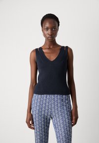 Marineblå strikket tanktop med V-hals og skulderutskjæringer, sammen med blå mønstrede bukser med geometriske design.