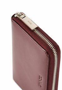 Bordowy skórzany portfel z teksturowanym materiałowym wykończeniem, srebrnym suwakiem i grawerowanym logo z przodu. Krawędzie są gładkie i prostokątne.