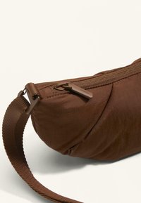 Borsa imbottita marrone dalla forma arrotondata, con chiusura a zip e tracolla intrecciata. Il materiale sembra liscio con un leggero splendore.