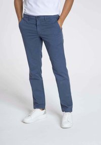 Des chinos en coton slim-fit de couleur bleue avec une taille plate, des poches latérales et une fermeture à bouton. Portés avec des baskets blanches pour un look décontracté.