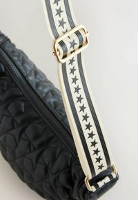 Fekete steppelt válltáska cipzáras záródással. Krémszínű pánttal, fekete csillagokkal és fémes arany hardveres díszítéssel.