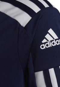 Maglietta sportiva di un blu navy con tre strisce bianche sulla spalla, tessuto strutturato e un prominente logo "adidas" bianco sul petto.