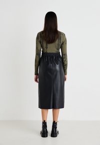 Haut à manches longues vert tie-dye associé à une jupe midi noire en simili cuir avec une taille élastique, porté avec des bottes noires chunky.