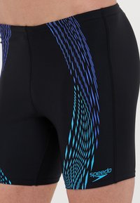 Čierne plavky s modro-fialovým diagonálnym vzorom. Vyrobené z elastického materiálu s plochými švami a logom Speedo na nohe.