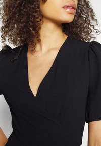 Black wrap dress with short puff sleeves, deep V-neckline, textured fabric, and subtle seams. Focus on neckline and sleeve details.