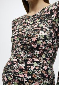 Φόρεμα με λουλουδάτο μοτίβο σε μαύρο φόντο, με υφή ριγμένη, μακριά μανίκια και εφαρμοστή σιλουέτα.