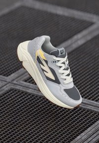 Gray athletic sneaker with a mesh upper, white and yellow accents, round toe, and textured rubber sole. Features a classic lace-up design.
