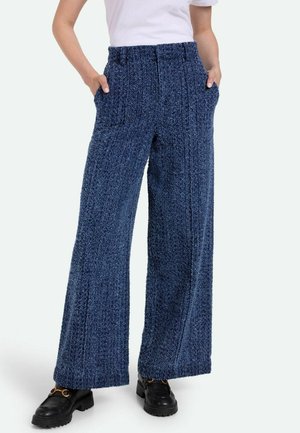 Breda blå texturerade byxor med sidofickor och hög midja, tillverkade av ett mjukt, mysigt material. Bärs med svarta chunky loafers.