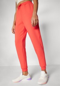 Koral joggebukser med snor i livet, tapered ben og ribbestrikkede mansjetter; kombinert med hvite sneakers med lilla detaljer.