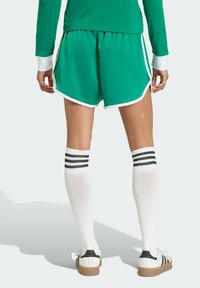 Green athletic shorts with white trim, paired with knee-high white socks featuring black stripes, and white sneakers with a black heel.