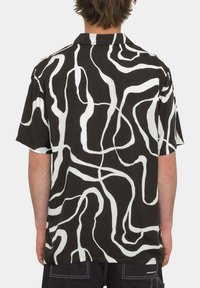 Camisa de manga corta en tela negra con un patrón ondulado abstracto en blanco. Cuello abotonado con un ajuste relajado. Sin marcas visibles.