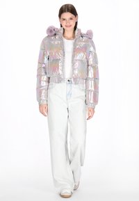 Srebrna błyszcząca krótka kurtka puchowa z kapturem, dwoma przednimi kieszeniami oraz fioletowymi akcentami z futerka syntetycznego. W zestawie z jasnymi dżinsami.