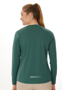 Langermige groene sportshirt met een gladde textuur, een ronde halslijn en reflecterende accentlijnen op de onderrug.