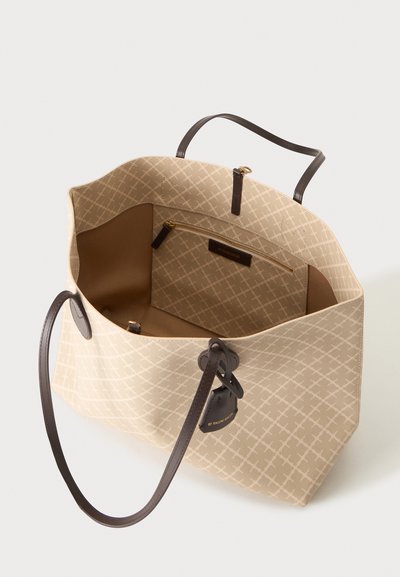Sac fourre-tout beige avec motif en croix, poignées marron foncé, poche intérieure zippée et étiquette de bagage assortie attachée à la poignée.