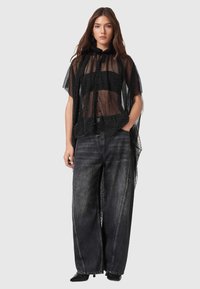 Czarna przezroczysta peleryna z subtelnymi połyskującymi detalami, zapinana na guziki, z kapturem. Noszona na luźnych, ciemnych dżinsach i czarnych, spiczastych butach.