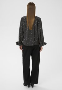 Grå bluse med hvide prikker, rynkede manchetter og rund halsudskæring, parret med sorte vide bukser og højhælede sko.