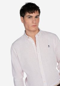 Camisa blanca de botones con rayas verticales rosas, con un pequeño logo bordado en azul marino en el pecho y un diseño de cuello clásico.