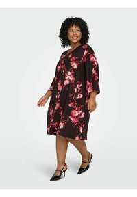 Smeđa cvjetna haljina s labavim krojem, ukrašena crvenim i ružičastim uzorcima cvijeća. Kratki rukavi i dizajn do koljena s glatkom teksturom.